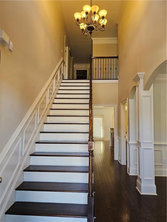 stairway with a notable chandelier, ornamental molding, wood finished floors, arched walkways, and a high ceiling