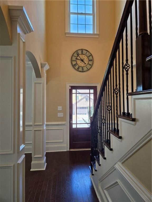 entrance foyer featuring wood finished floors, a wainscoted wall, a high ceiling, arched walkways, and a decorative wall