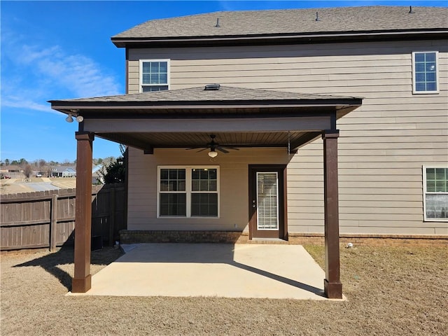 view of exterior entry featuring a ceiling fan, a patio, fence, and a shingled roof