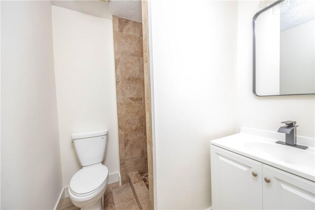 bathroom with a shower, a textured ceiling, vanity, and toilet