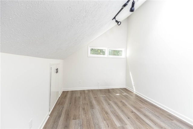 additional living space featuring a textured ceiling, light wood-type flooring, and vaulted ceiling