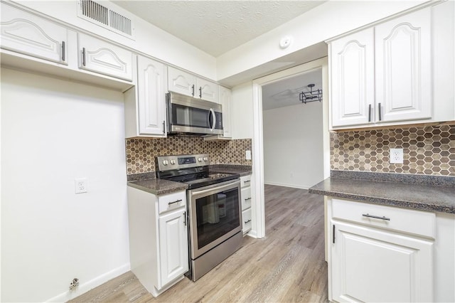 kitchen with backsplash, white cabinets, a textured ceiling, appliances with stainless steel finishes, and light hardwood / wood-style floors