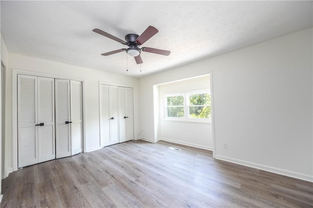 unfurnished bedroom with a textured ceiling, two closets, light hardwood / wood-style flooring, and ceiling fan