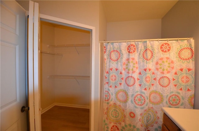 full bath featuring a spacious closet, vanity, baseboards, and wood finished floors