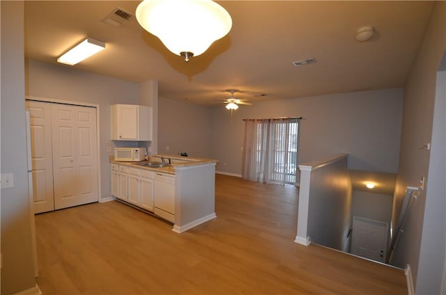 kitchen with white cabinetry, a peninsula, light wood finished floors, and white appliances