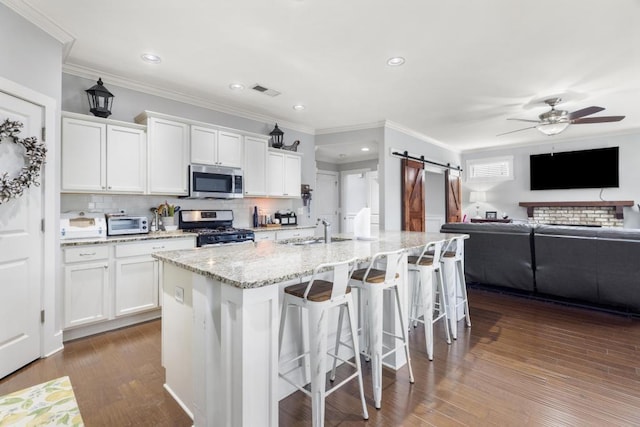 kitchen with stainless steel appliances, a barn door, a center island with sink, and white cabinets