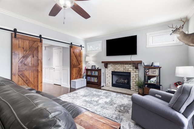 living room with a fireplace, hardwood / wood-style flooring, ceiling fan, crown molding, and a barn door