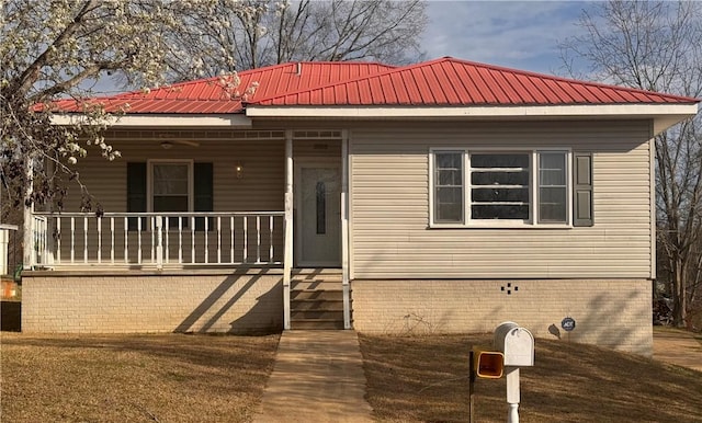 view of front of property featuring a porch, brick siding, and metal roof