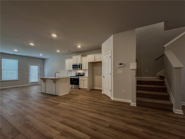 kitchen featuring dark wood-style flooring, light countertops, appliances with stainless steel finishes, white cabinets, and a kitchen island with sink