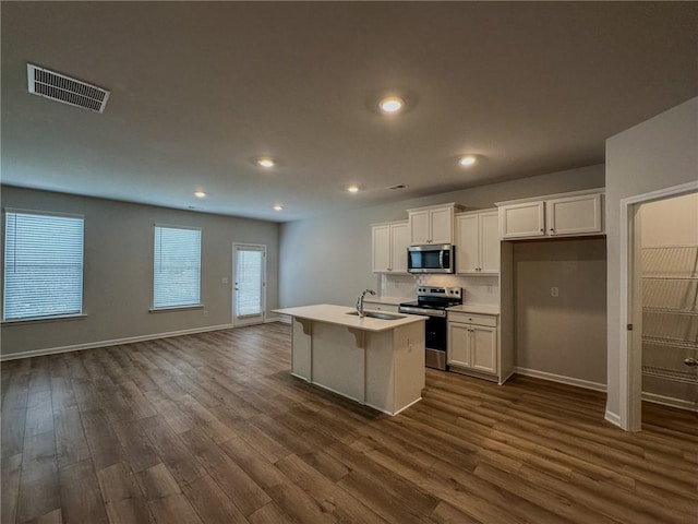 kitchen featuring visible vents, light countertops, appliances with stainless steel finishes, dark wood-style floors, and an island with sink