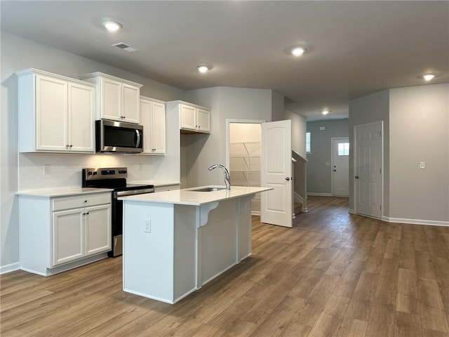 kitchen with visible vents, appliances with stainless steel finishes, a kitchen island with sink, light countertops, and white cabinetry