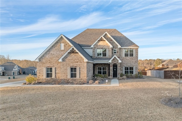 view of front facade with stone siding, roof with shingles, fence, and brick siding