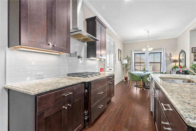 kitchen with wall chimney exhaust hood, light stone counters, ornamental molding, dark wood-style flooring, and a sink