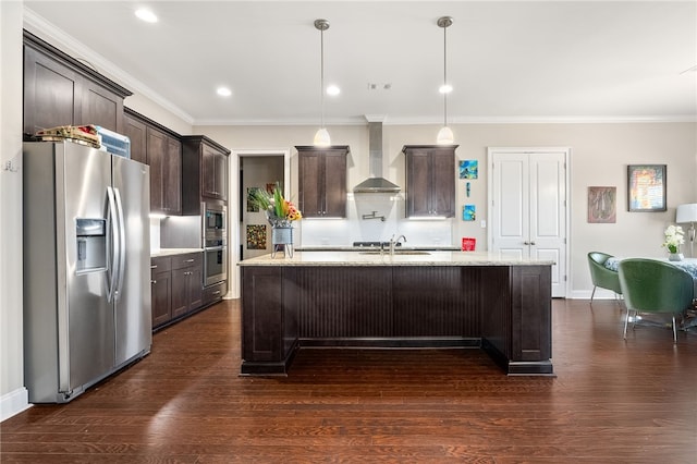 kitchen with light stone counters, a kitchen island with sink, appliances with stainless steel finishes, wall chimney exhaust hood, and pendant lighting