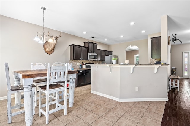 kitchen with decorative backsplash, appliances with stainless steel finishes, a breakfast bar, a chandelier, and recessed lighting