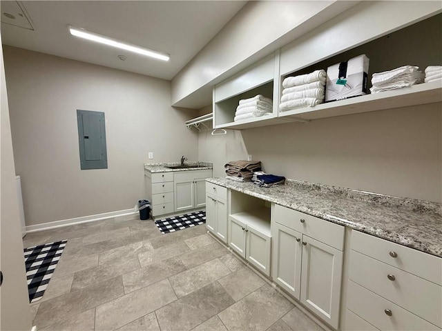 clothes washing area featuring electric panel, baseboards, and a sink