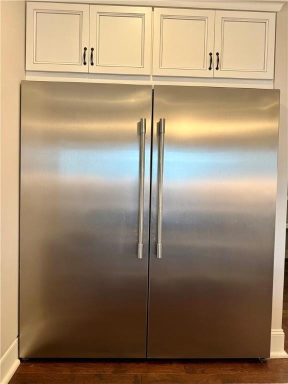 kitchen view of built in fridge, white cabinetry, and dark wood-type flooring