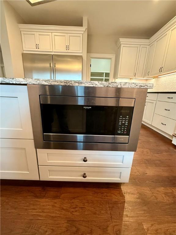 kitchen view of stainless steel microwave, white cabinetry, and dark wood-type flooring