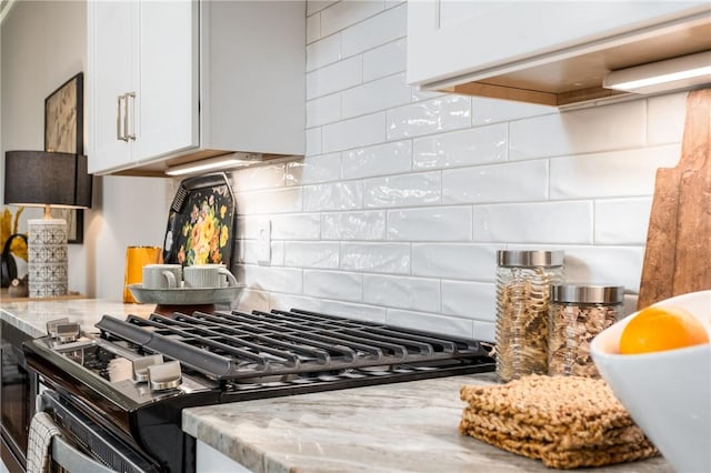 kitchen with stainless steel range with gas stovetop, light stone counters, white cabinets, and decorative backsplash