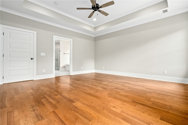 empty room featuring light wood-style floors, a raised ceiling, visible vents, and baseboards