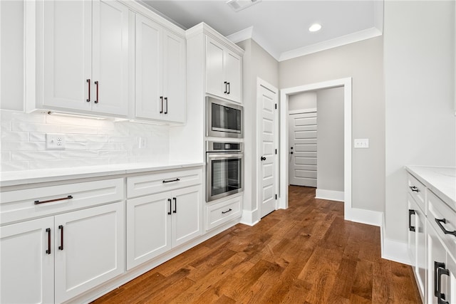 kitchen with dark wood-style floors, crown molding, backsplash, built in microwave, and oven