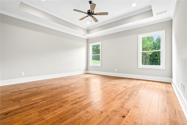 spare room featuring light wood-style floors, a raised ceiling, visible vents, and baseboards