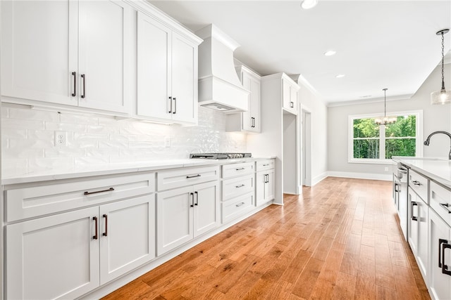 kitchen featuring white cabinets, light wood-style flooring, custom range hood, stainless steel gas cooktop, and backsplash