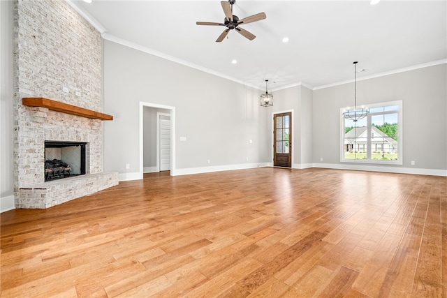 unfurnished living room featuring light wood-style flooring, a fireplace, ornamental molding, and ceiling fan with notable chandelier