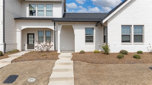 entrance to property with covered porch, brick siding, and roof with shingles