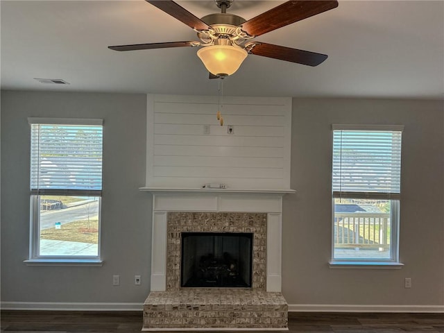 unfurnished living room with visible vents, baseboards, a fireplace with raised hearth, and dark wood finished floors