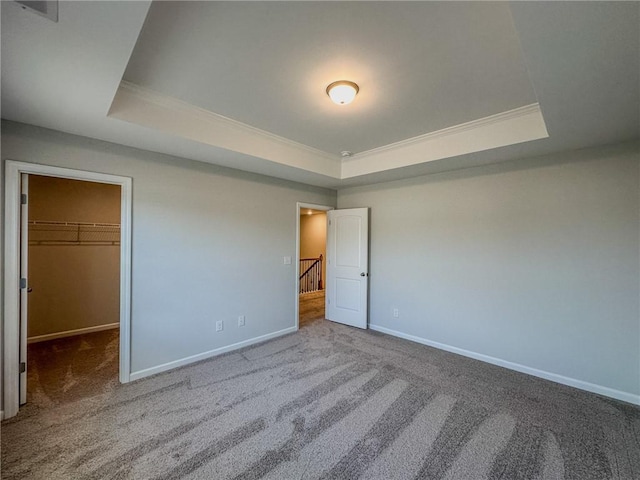 unfurnished bedroom featuring a walk in closet, a tray ceiling, baseboards, and carpet floors