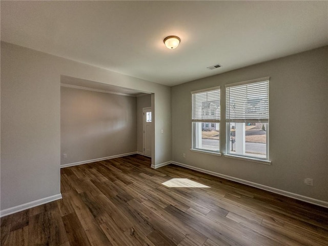 unfurnished room featuring visible vents, baseboards, and dark wood-style flooring