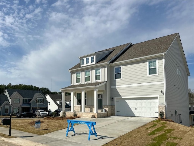 view of front of home featuring roof with shingles, an attached garage, covered porch, concrete driveway, and stone siding