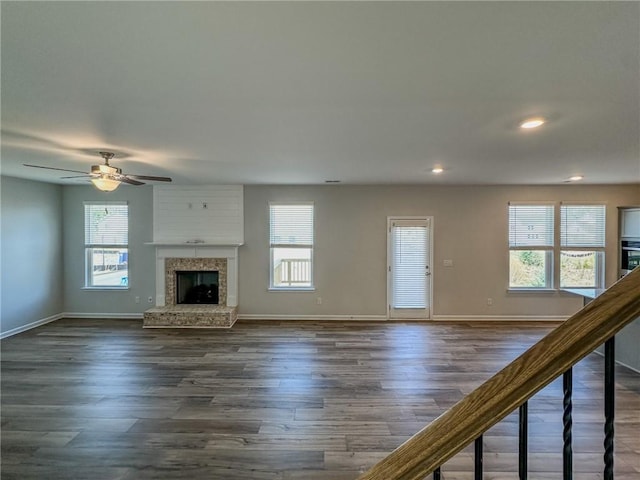 unfurnished living room featuring dark wood-style floors, plenty of natural light, and a fireplace with raised hearth