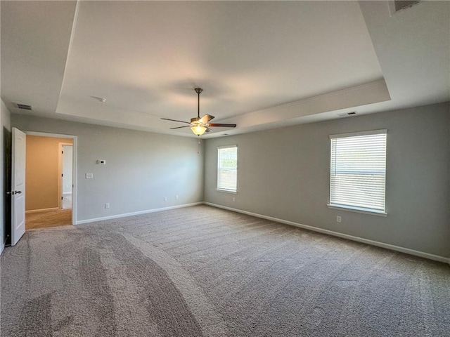 carpeted empty room featuring visible vents, ceiling fan, baseboards, and a tray ceiling