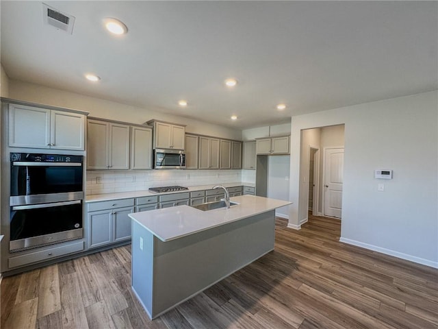 kitchen featuring visible vents, a sink, dark wood-type flooring, appliances with stainless steel finishes, and tasteful backsplash