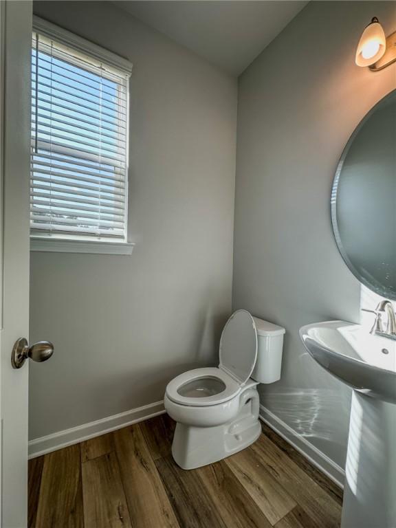 half bath featuring a sink, baseboards, toilet, and wood finished floors