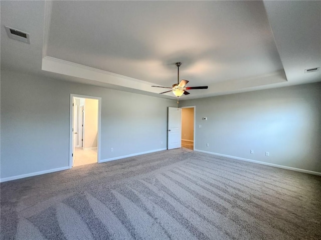 carpeted empty room with visible vents, a raised ceiling, and baseboards