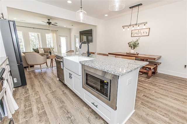 kitchen featuring stainless steel appliances, white cabinetry, ceiling fan, hanging light fixtures, and a kitchen island with sink