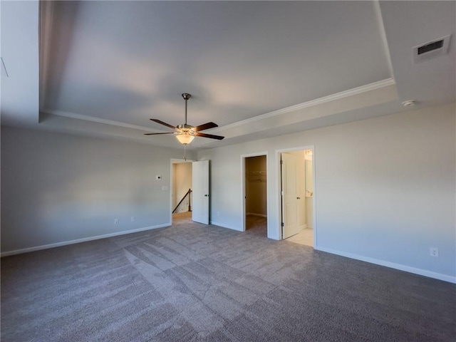 unfurnished bedroom with a spacious closet, a tray ceiling, a closet, and ceiling fan