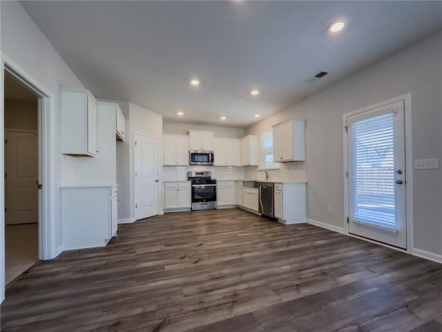 kitchen with dark wood-type flooring, appliances with stainless steel finishes, white cabinets, and tasteful backsplash