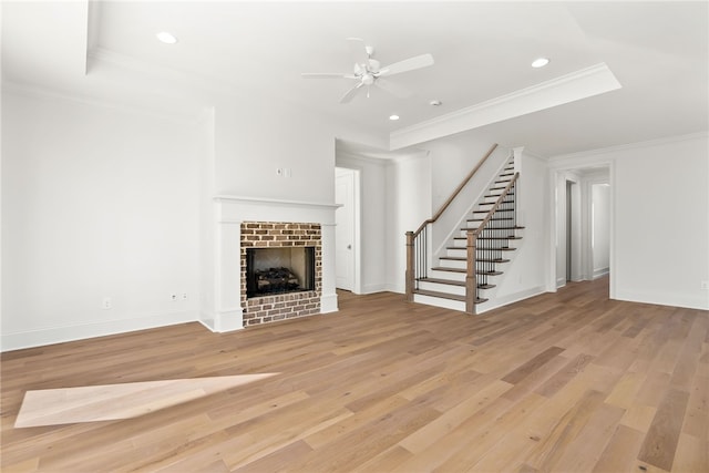 unfurnished living room with crown molding, a brick fireplace, ceiling fan, a tray ceiling, and light hardwood / wood-style floors