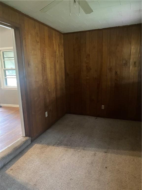 unfurnished room with ceiling fan, light colored carpet, and wooden walls