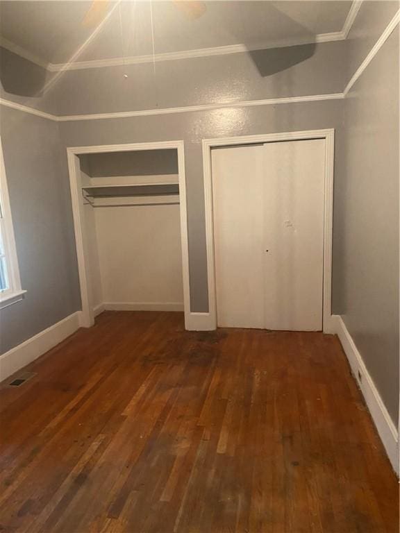 unfurnished bedroom with dark hardwood / wood-style floors, ornamental molding, and two closets