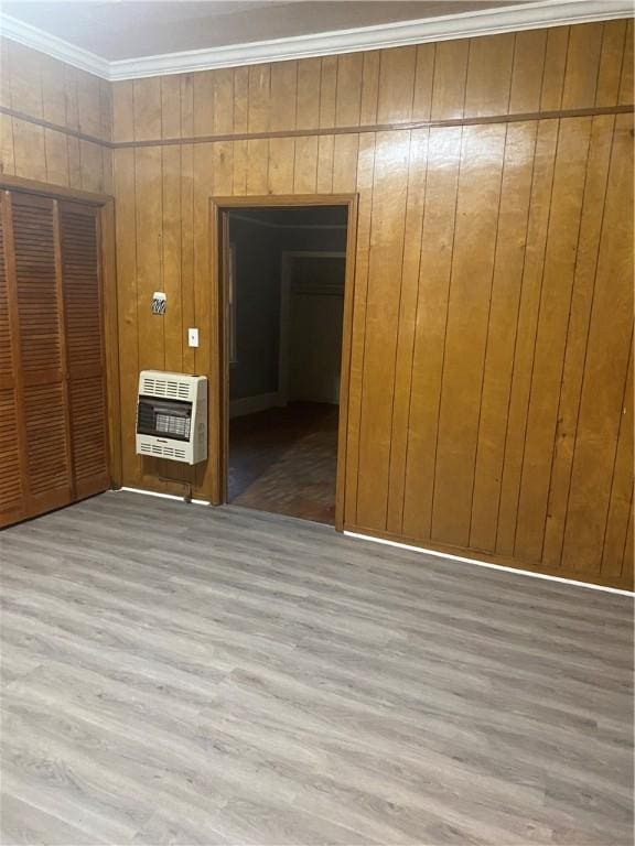 empty room with wood-type flooring, heating unit, ornamental molding, and wood walls