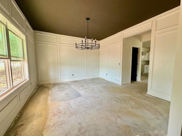 unfurnished dining area featuring a decorative wall, concrete floors, and a notable chandelier