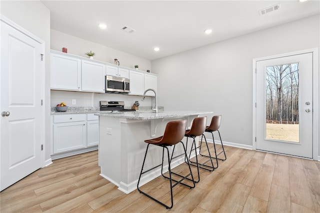 kitchen featuring visible vents, a breakfast bar, light wood-style flooring, stainless steel appliances, and a kitchen island with sink