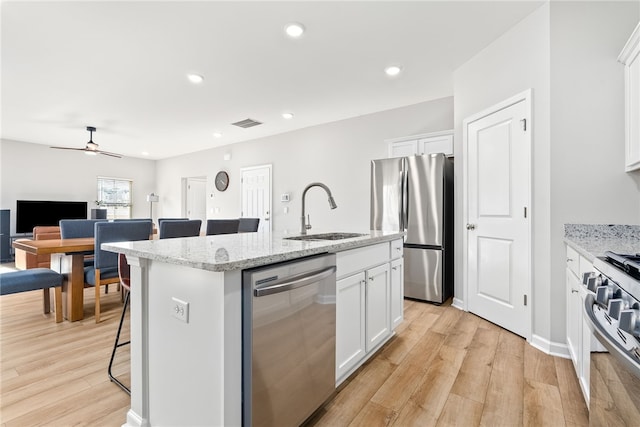 kitchen with an island with sink, light wood-type flooring, stainless steel appliances, white cabinetry, and a sink