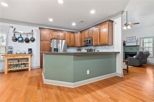 kitchen with decorative backsplash, ceiling fan, light wood-type flooring, appliances with stainless steel finishes, and kitchen peninsula