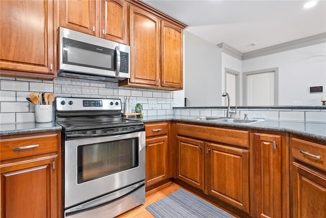 kitchen with backsplash, sink, dark stone countertops, ornamental molding, and stainless steel appliances